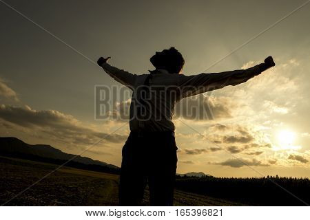 Low angle three quarter body view of silhouetted person with spread arms in countryside sunset freedom concept.