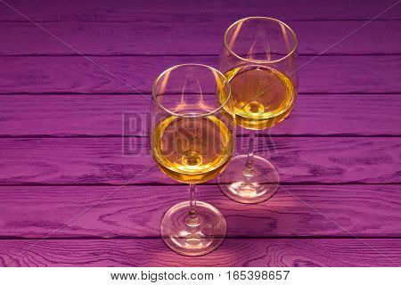 White wine in the wineglass on the purple wood background
