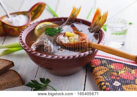 Traditional Russian fish soup in a clay bowl on a wooden table. Rustic style