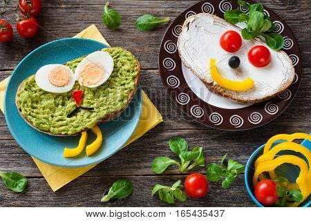 Funny colorful creative meal idea for kids: avocado sandwich with hard boiled egg, pepper nose and black olive mustage; cream cheese sandwich with vegetable face and corn salad 