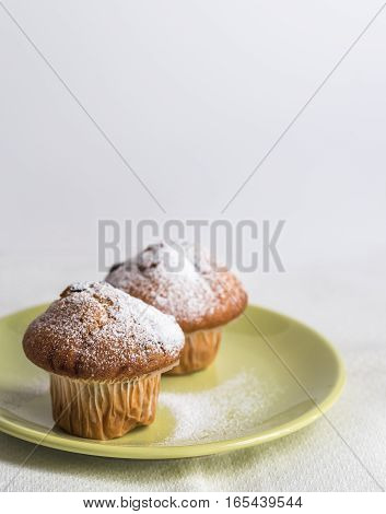 Two muffins by powdered sugar on green plate.