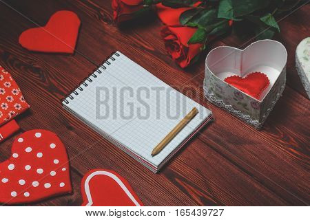 Opened mock up notepad, toy hearts and red roses on wooden table. Romantic template. Valentines day concept. Toned image