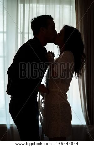 Couple kissing near window. People undressing each other. Ignite the fire of passion.