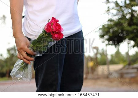 Woman holding bouquet of beautiful red roses on nature bokeh background. Romance and sweet Valentine's day concept