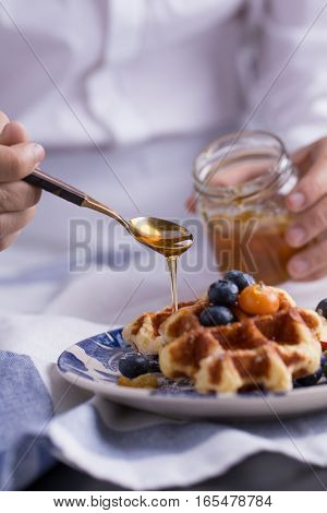 Blueberry apple waffle with honey set on a dish with a chef's hand holding spoon for a jar of honey ready to serve.