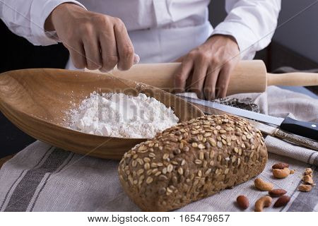 Whole grain bread put on kitchen napkin decorated with almond with a chef holding dough roller at the background.