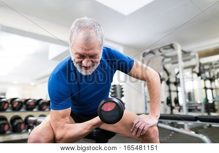 Senior man in sports clothing in gym working out with weights.