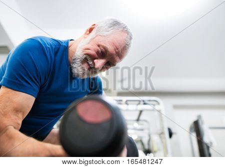 Senior man in sports clothing in gym working out with weights.