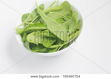 Arugula Leaves into a bowl over a white background