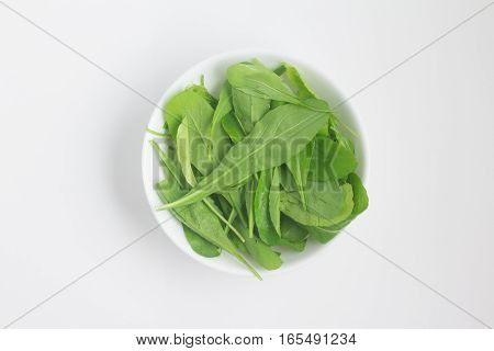 Arugula Leaves into a bowl over a white background