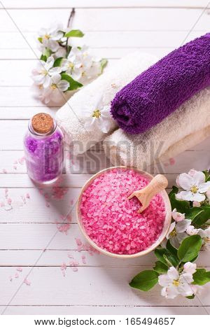 Spa setting. Sea salt in bowl towels and flowers on white wooden background. Selective focus. Place for text.Vertical image.