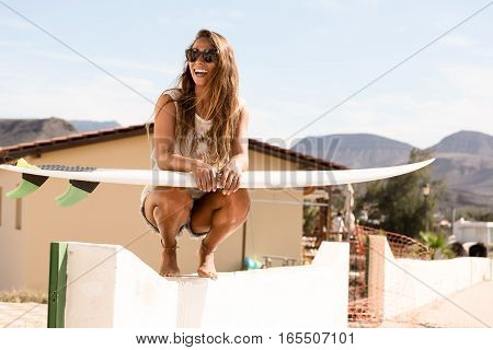 girl squats on wall with a surfboard
