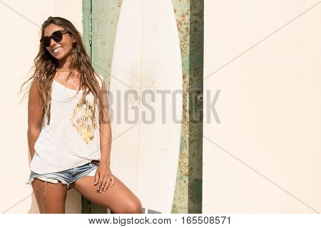 young girl stand with a surfboard in front of grunge door.