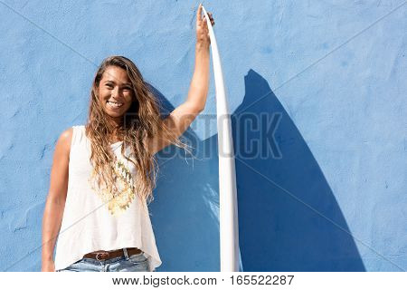 surfer girl with surfboard in front of blue wall