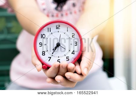 Holding red clock on hand and giving this to you with garden background.