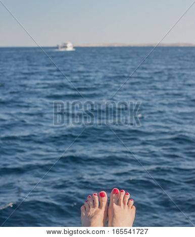 wooman feet with red nails on blue sea background