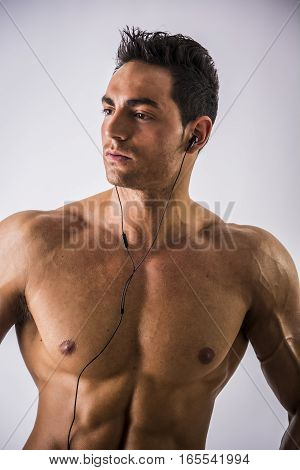 Attractive young man with muscular naked body listening to music with earphones, isolated on white background