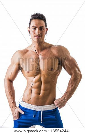 Attractive young man with muscular naked body listening to music with earphones, isolated on white background