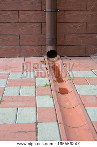 Rain gutter downspout pipe for roof runoff with open water drainage in the pavement.