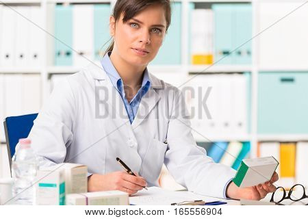 Female Pharmacist Sat At Desk Writing Notes