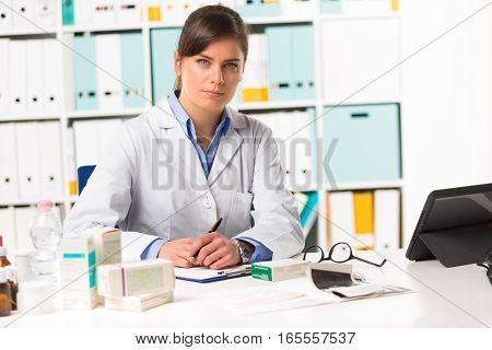 Female Pharmacist Sat At Desk Writing Notes