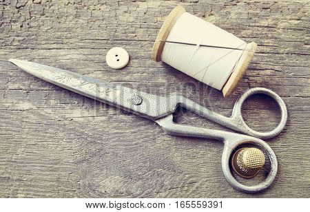 Vintage Background with sewing tools.Sewing kit. Scissors,button,bobbin with thread,needle and thimble on the old wooden background.