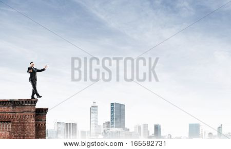 Businessman with blindfolder on eyes walking on building top