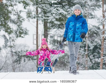 Happy boy and girl riding sled and having fun. Children play outdoors in snow - sledding. Kids sled in snowy park in winter. Outdoor fun for family Christmas vacation.