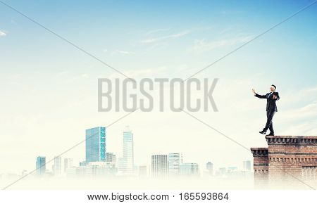 Businessman with blindfolder on eyes walking on building top