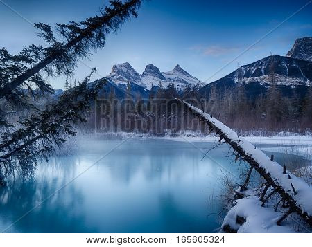 Sunrise view of the Three Sisters from a frozen Policemen's Creek along the Bow River outside Canmore, Alberta in winter.