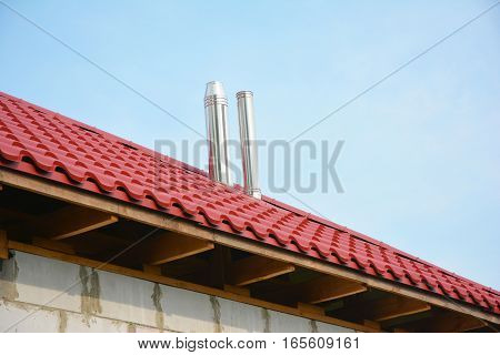 Roofing Construction Exterior. Building new house with metal red roof and steel chimney outdoor. Soffit and Fascia unfinished installation.