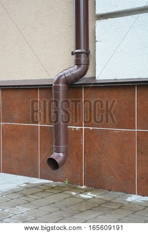 House Wall Facade with Rain Gutter Plastic Pipeline Drainage Downspout System and Pavement near Home Foundation Outdoor.