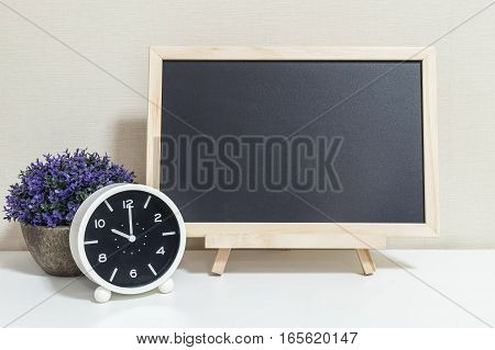 Closeup alarm clock for decorate show 10 o'clock with wood black board on white wood desk and cream wallpaper textured background selective focus at the clock