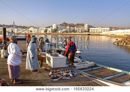 MUSCAT, OMAN - FEBRUARY 11, 2012: Fishermen at The Muttrah Fish docks early morning with Muttrah corniche in the Background