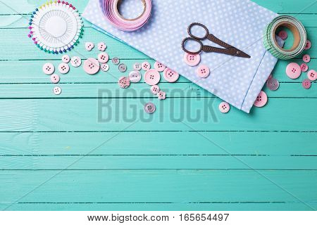 Sewing thread - buttons scissors fabric on turquoise wooden background. Selective focus. Scrapbboking. Flat lay. Place for text.
