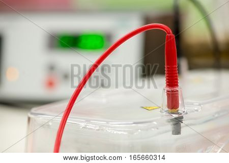 Close-up detail of a red wire from one of the electrical terminals of an agarose gel electrophoresis chamber. Gel electrophoresis is used to diagnose genetic diseases cancers and for research.