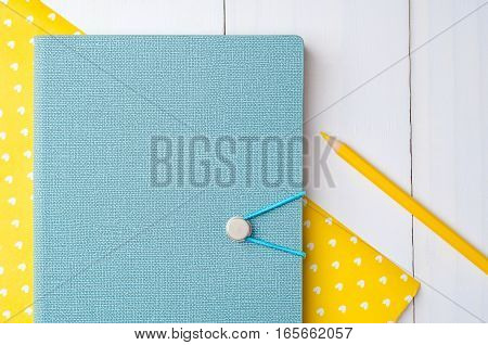 Blue notebook with color pencils on yellow paper and white wooden background