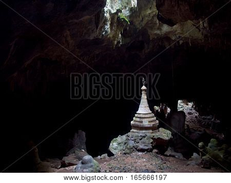 A lone Buddhist stupa is illuminated by a natural skylight in a dark cave in Myanmar