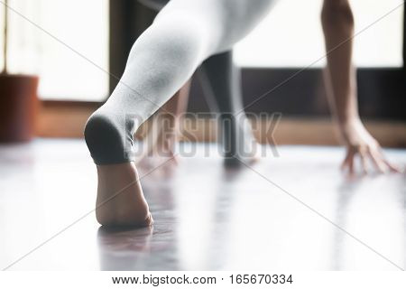 Close up of female stretched barefoot leg in sportswear, grey yoga pants with heel cover for practicing yoga, working out, indoor, home interior background. Back view