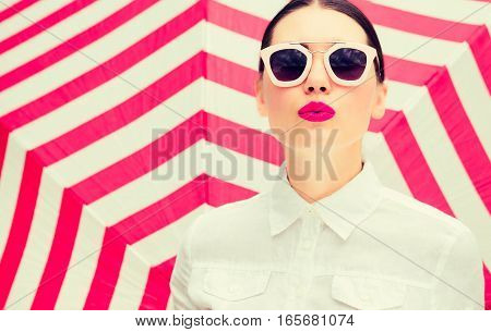 Fashion portrait of a beautiful woman wearing white chemise and sunglasses with bright painted lips next to a striped background