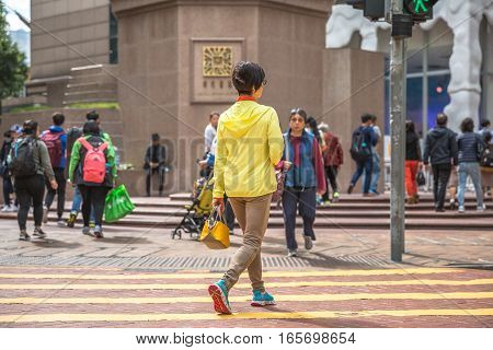 Hong Kong, China - December 6, 2016: Typical Asian woman in yellow along intersection in Times Square.Causeway bay is one of most attractive areas for tourists visiting Hong Kong and good for shopping