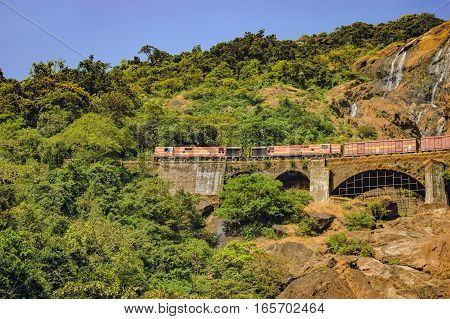 Goa, India - November 16, 2012: Train on the railroad bridge in the background of Dudhsagar Waterfall.