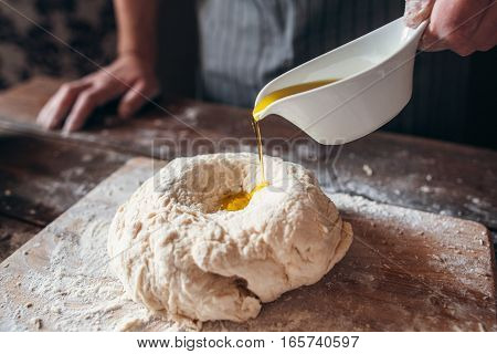 Adding olive oil to raw dough close-up. Baker preparing pastry for bread with all ingredients. Traditional bakery recipe, kitchen, cooking concept