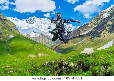 USHGULI GEORGIA - MAY 22 2016: The young Georgian man performs the jump element from the ethnic war dance in the national costume on May 22 in Ushguli.