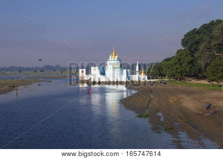 Buddhist temple at sunrise reflecting in lake and Local Fishermen near U bein bridge at Amarapura Mandalay Myanmar.