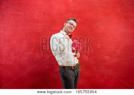 Young beautiful man with flowers on red studio background