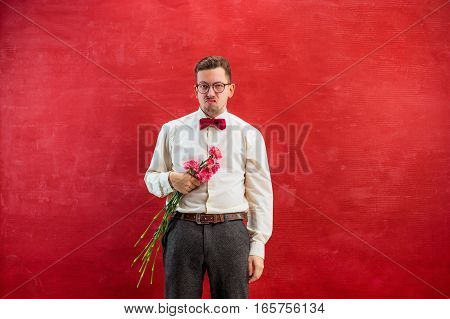 Young beautiful man with flowers on red studio background