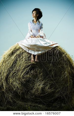 Piękna kobieta w sukienka vintage siedzi na stogu siana