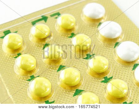 close-up yellow white oral contraceptive pills in golden aluminum blister foil packaging with green arrow instruction on white background, use of birth control pills to prevent pregnancy for women