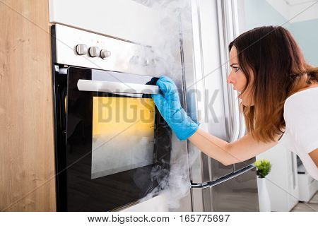 Shocked Young Woman Looking At Smoke Coming Out Of Oven In Kitchen